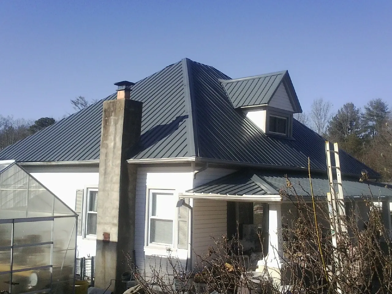 Dark blue standing seam metal roof on a white farmhouse with dormer — Slate & Tile Roof Repair by Roofing Brothers in North Haverhill