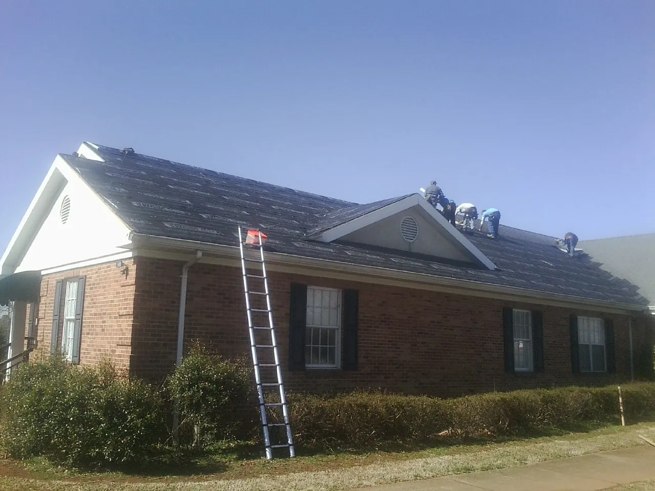 Crew tearing shingles off a brick ranch roof with a ladder set — Emergency Roof Repair work by our crew in North Haverhill