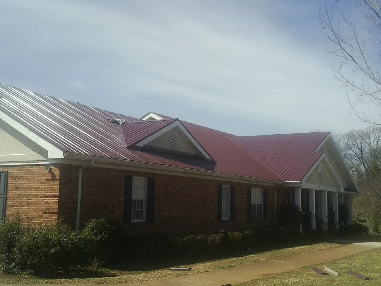 Red metal roof with gabled entries on a long brick building, from a Hail Damage Roof Repair job in North Haverhill