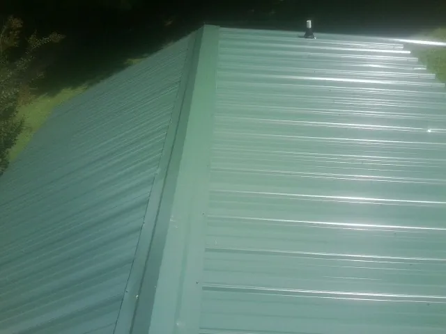 New green metal panels meeting at the ridge of a roof — Flat Roof Repair work by our crew in North Haverhill