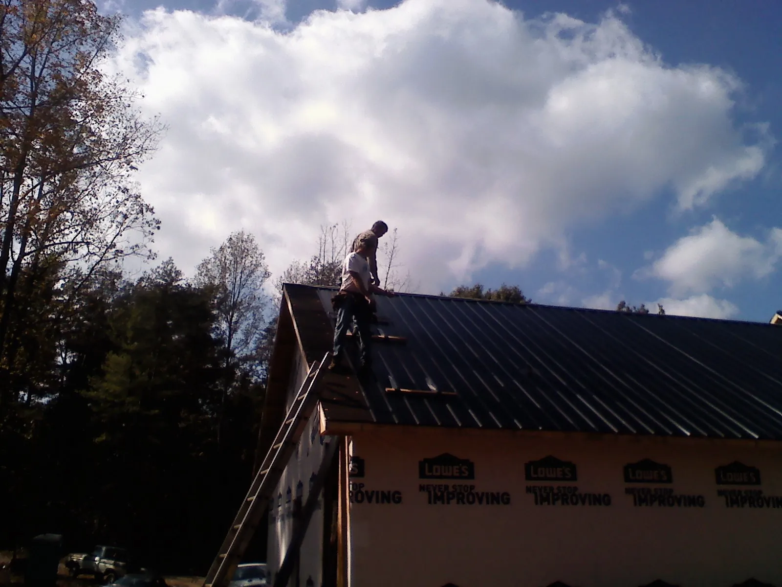 Roofer fastening dark metal panels high against a cloudy sky, from a Roof Inspection job in North Haverhill