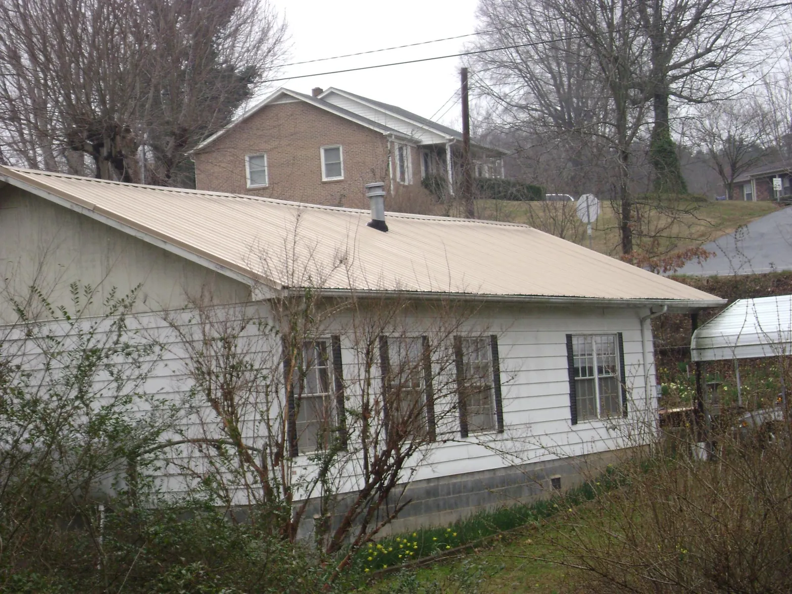Tan metal roof on a white sided house set into a hillside — Commercial Roofing by Roofing Brothers in North Haverhill