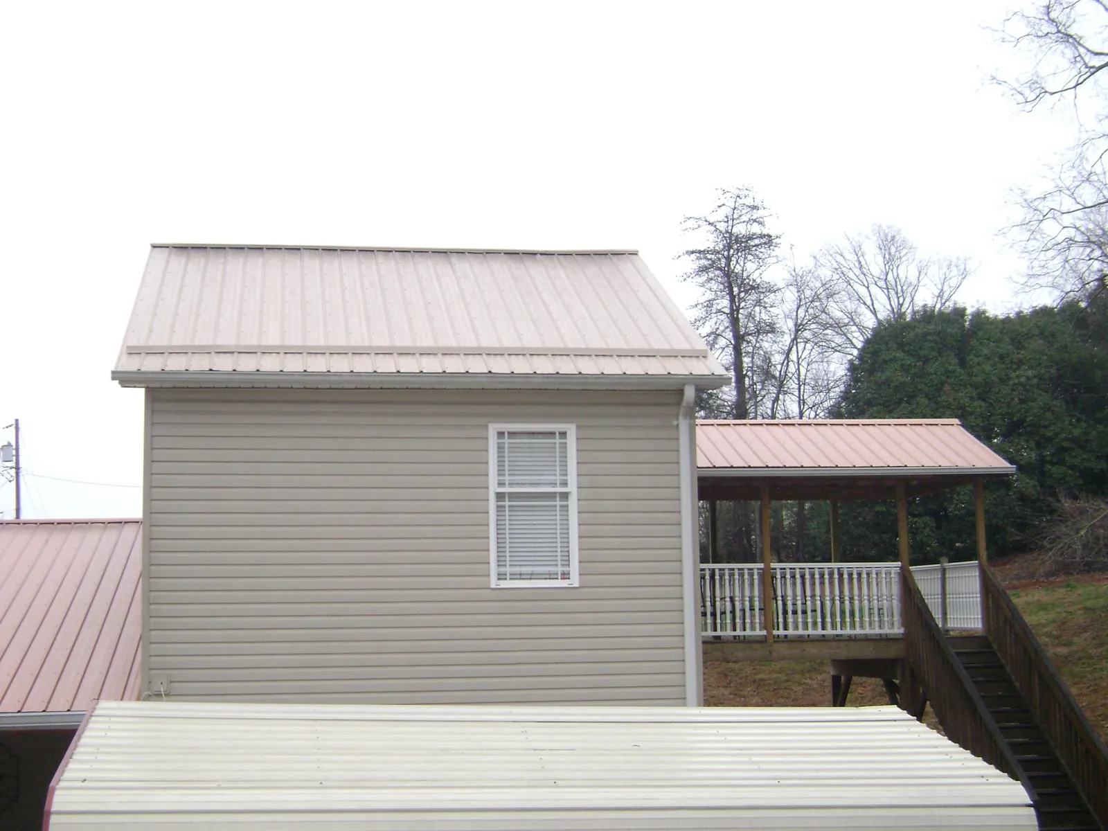 Tan metal roofs on a two story addition and attached porch, from a Roof Replacement job in North Haverhill
